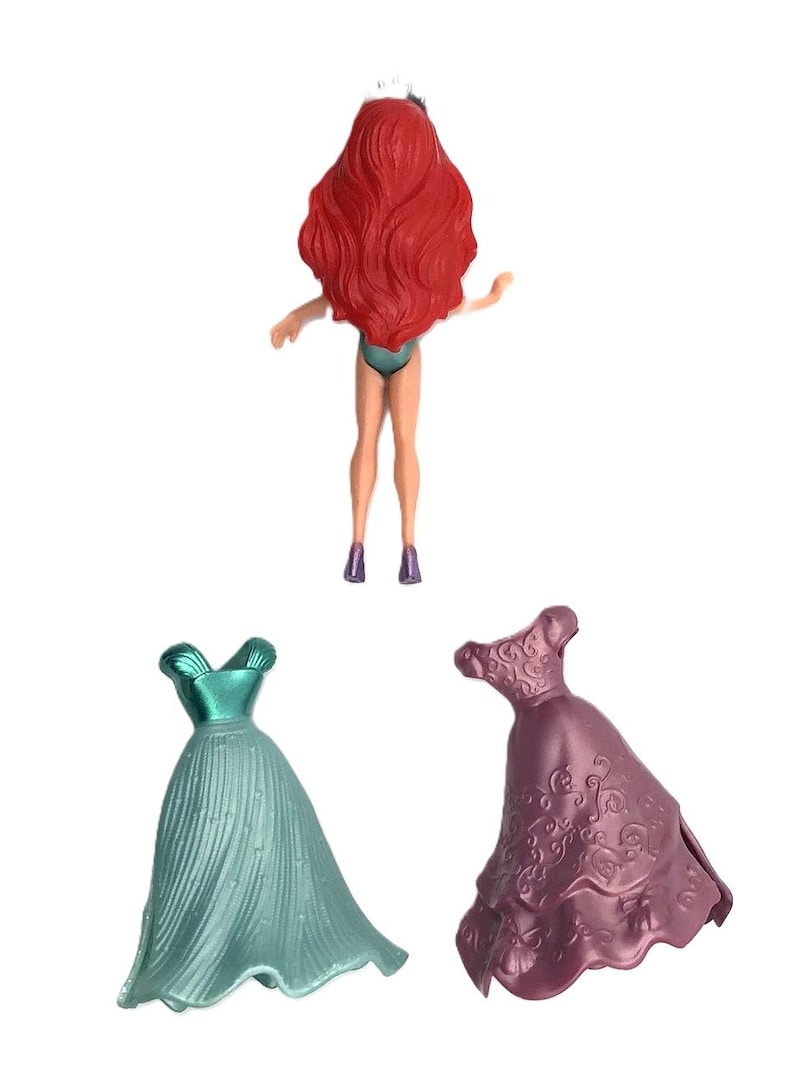 May include: A red-haired doll with a crown, wearing a teal swimsuit, and two dresses. One dress is teal and the other is purple with a floral pattern.