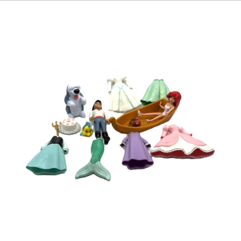Op de afbeelding: Een verzameling Disney-beeldjes en accessoires, waaronder Ariel in een boot, een zeemeerminstaart, jurken en andere personages. De beeldjes zijn in verschillende kleuren, waaronder blauw, groen en roze.