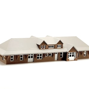 May include: A brown wooden model train station with a white roof and windows. The station has a front porch with a door and windows.