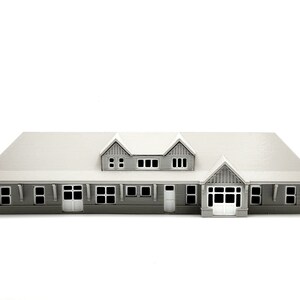 May include: A gray 3D printed model of a house with a gabled roof and multiple windows. The house has a front porch with a door and a set of windows.