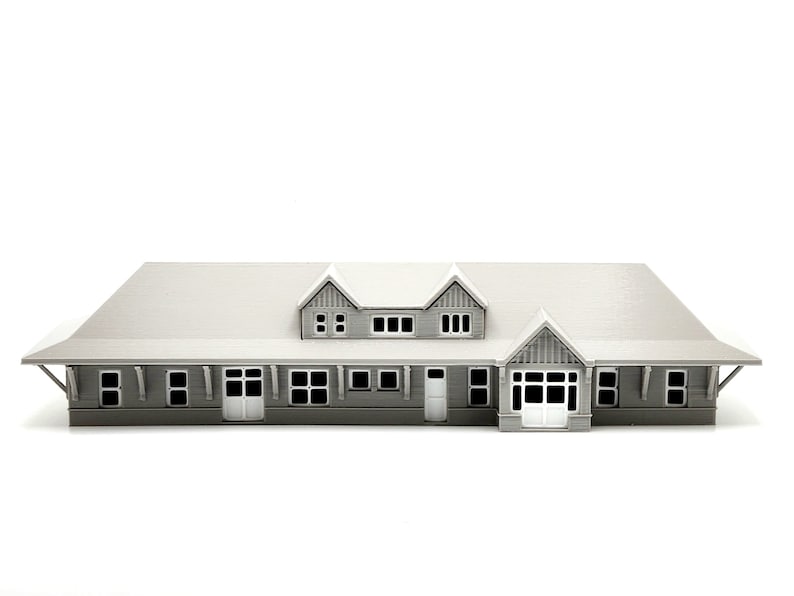May include: A gray 3D printed model of a house with a gabled roof and multiple windows. The house has a front porch with a door and a set of windows.