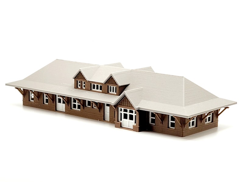 May include: A brown and white model train station with a gabled roof and multiple windows.