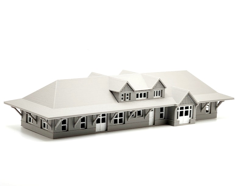 May include: A gray 3D printed model of a building with a gabled roof and multiple windows. The building has a porch with a railing and a door.