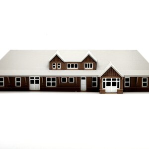 May include: A brown wooden model of a house with a white roof and multiple windows. The house has a front door and a porch.