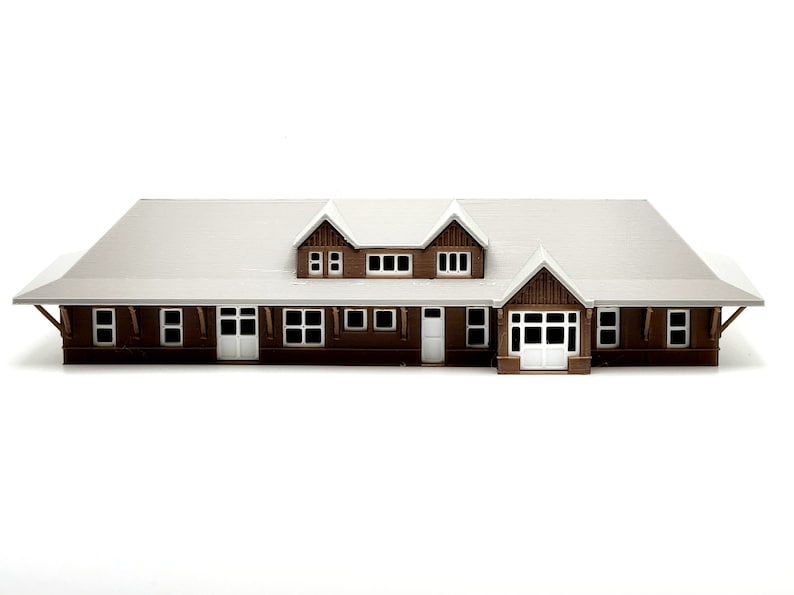 May include: A brown wooden model of a house with a white roof and multiple windows. The house has a front door and a porch.
