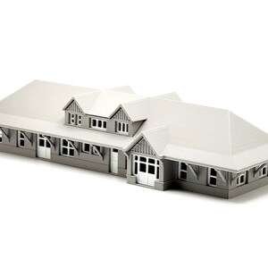 May include: A gray model train station with a gabled roof and multiple windows. The station has a covered platform and a small entrance.