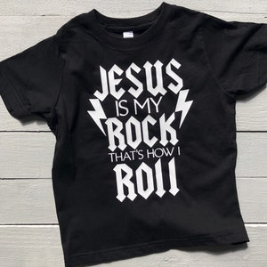 May include: Black t-shirt with white text that reads "Jesus is my rock, that's how I roll".