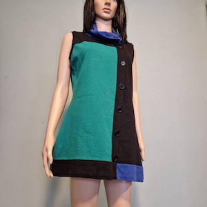 May include: A sleeveless dress with a black, teal and blue colour block design. The dress has a mock neck and a button closure down the front.