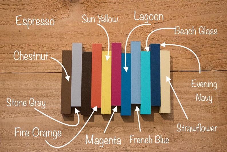 May include: A set of ten paint color samples, arranged horizontally on a wood surface. The colors are: Stone Gray, Chestnut, Espresso, Fire Orange, Magenta, Sun Yellow, Lagoon, French Blue, Evening Navy, and Strawflower.