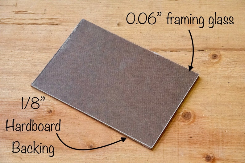 May include: A close-up of a 1/8" hardboard backing and a 0.06" framing glass. The hardboard is brown and the glass is clear.
