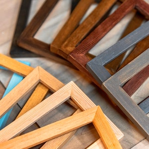 May include: A collection of wooden picture frames in various colors, including natural wood, brown, blue, and gray. The frames are arranged in a fan shape, with the largest frame at the bottom and the smallest frame at the top.