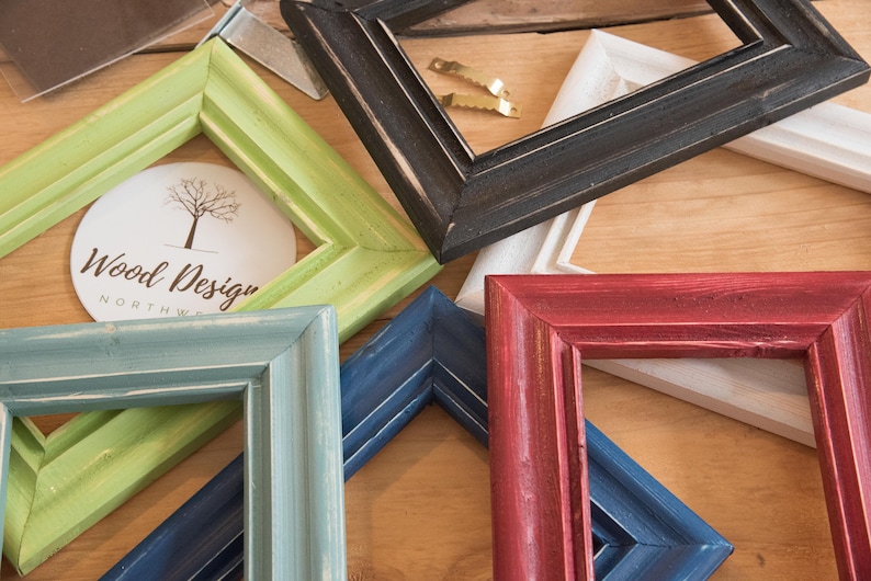 May include: Assortment of wooden picture frames in various colors, including green, blue, red, black, and white. The frames are arranged on a wooden surface. The frames are all different sizes and have a rustic, distressed look. The frames are perfect for displaying photos, artwork, or other mementos.
