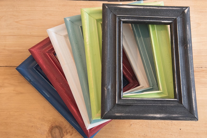 May include: A set of six picture frames in various colors, including black, green, blue, red, white, and gray. The frames are stacked on top of each other, with the black frame on top.