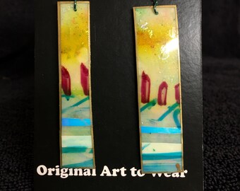 May include: A pair of rectangular earrings with a yellow, red, and blue abstract design. The earrings are made of metal and have a wire hook closure. The earrings are displayed on a black card with the text "RC Robert Cerins Designs" and "Original Art to Wear".