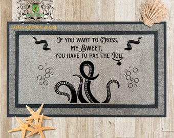 May include: Gray rectangular doormat with a dark gray border. The mat features the text "If you want to cross, my sweet, you have to pay the toll" and a black octopus design. Decorative seashells and starfish are also present.