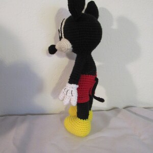 May include: A black and white crocheted Mickey Mouse doll with red shorts and yellow shoes. The doll is standing on a white surface.