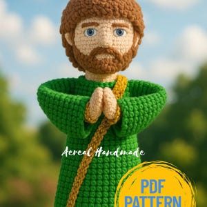Puede incluir: Muñeco de ganchillo con cabello y barba castaños, ojos azules y una túnica verde. El muñeco tiene las manos juntas en oración y una faja dorada. La imagen incluye el texto "Aereal Handmade" y "PDF PATTERN ONLY".