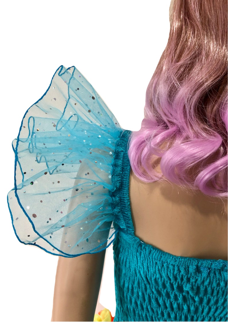 Pode incluir: Um vestido turquesa com uma manga de tule azul com babados e brilho. O vestido tem um decote quadrado e um corpete justo.