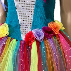 Pode incluir: Um vestido turquesa e branco com uma saia de tule arco-&iacute;ris e enfeites florais. O corpete &eacute; decorado com lantejoulas.
