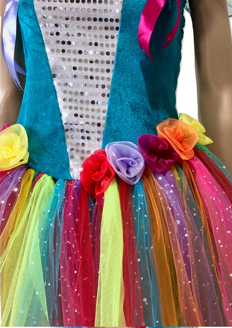 Pode incluir: Um vestido turquesa e branco com uma saia de tule arco-&iacute;ris e enfeites florais. O corpete &eacute; decorado com lantejoulas.