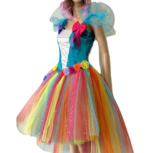 Pode incluir: Um vestido de tule arco-&iacute;ris colorido com um corpete turquesa e um detalhe de flores. O vestido tem uma bainha alta-baixa e &eacute; decorado com glitter.
