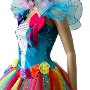 Pode incluir: Um vestido turquesa e branco com uma saia de tule arco-&iacute;ris e detalhes de flores coloridas. O vestido tem um la&ccedil;o rosa e babados de tule azul nos ombros.