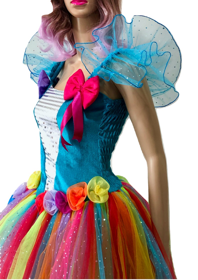 Pode incluir: Um vestido turquesa e branco com uma saia de tule arco-&iacute;ris e detalhes de flores coloridas. O vestido tem um la&ccedil;o rosa e babados de tule azul nos ombros.