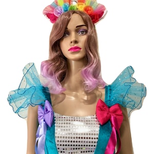Pode incluir: Um vestido de lantejoulas turquesa e prata com babados de tule arco-&iacute;ris nos ombros e uma faixa de cabe&ccedil;a de unic&oacute;rnio com flores arco-&iacute;ris.