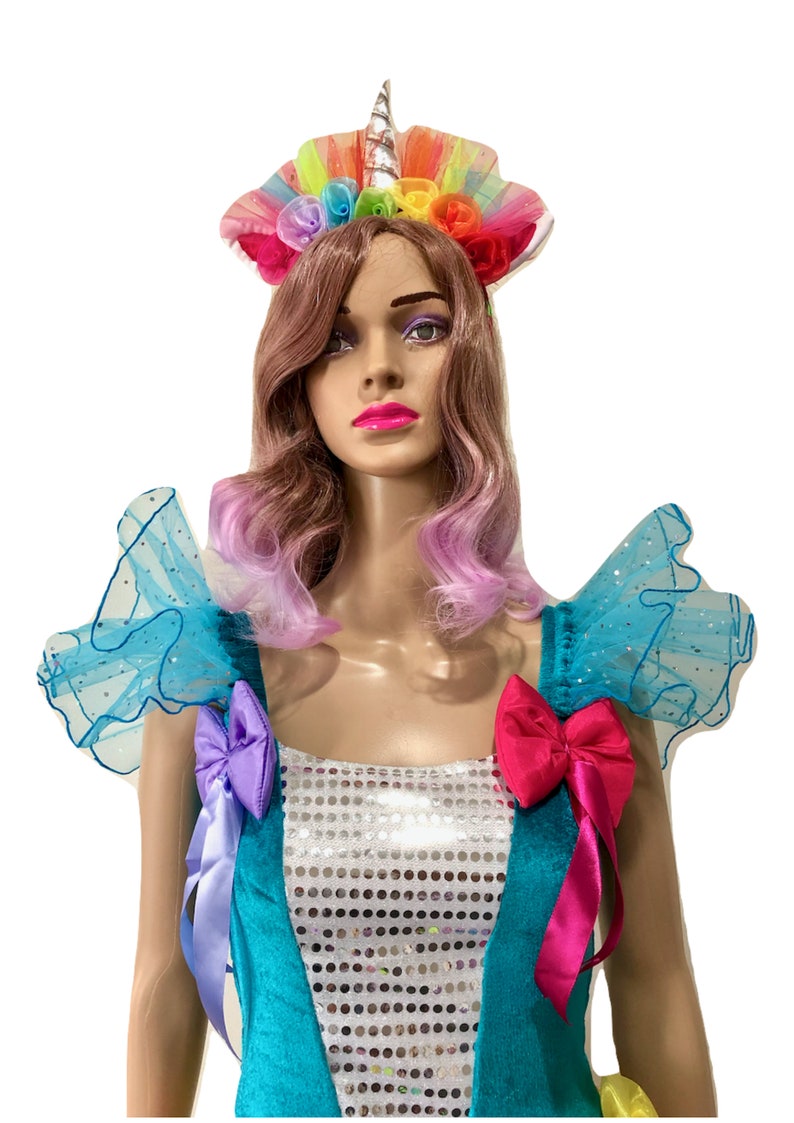 Pode incluir: Um vestido de lantejoulas turquesa e prata com babados de tule arco-&iacute;ris nos ombros e uma faixa de cabe&ccedil;a de unic&oacute;rnio com flores arco-&iacute;ris.