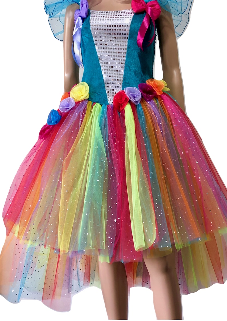 Pode incluir: Um vestido de tule arco-&iacute;ris com um corpete turquesa e detalhes de lantejoulas. O vestido tem uma bainha alta-baixa e &eacute; decorado com flores de tecido coloridas.