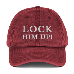 May include: A red vintage baseball cap with the text "LOCK HIM UP!" embroidered in white.