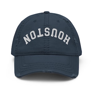 May include: A distressed navy blue baseball cap with the word "HOUSTON" arched across the front in white lettering. The cap has a pre-worn look with frayed edges.