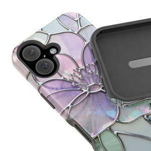 May include: A smartphone case with a floral design. The case features a stained-glass style flower in shades of purple, pink, and green, outlined with silver-coloured metal. The phone's camera lenses are visible. The case is partially open, revealing the black interior.