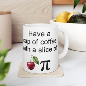 May include: White ceramic coffee mug with a black graphic that reads "Have a cup of coffee with a slice of pi". A red cherry with a green leaf is next to the pi symbol.