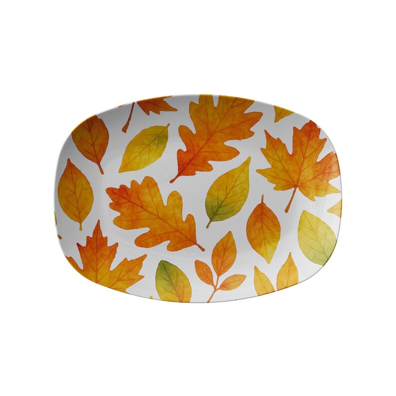May include: An oval serving platter with a white background and a pattern of autumn leaves in shades of yellow, orange, and green. The leaves are of various shapes and sizes, creating a seasonal design. The platter is perfect for serving food.