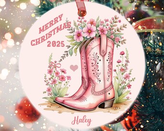 Puede incluir: Adorno navideño redondo con un diseño de botas de vaquero rosas. El adorno presenta el texto "MERRY CHRISTMAS 2025" y el nombre "Haley". Las botas están llenas de flores rosas y vegetación.
