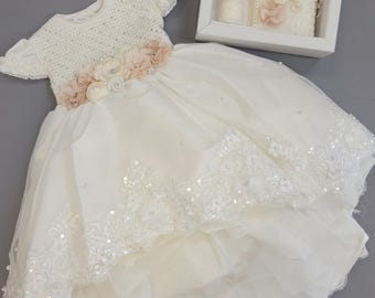 Peut inclure: Robe de bébé blanche avec une ceinture florale et un bandeau assorti. La robe a un corsage perlé et une jupe à plusieurs épaisseurs avec des détails en dentelle et en sequins. Une boîte blanche contient une bougie, un livre et d'autres accessoires de baptême.