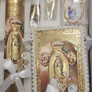 May include: A set of religious baptism items featuring a white candle with gold trim, a gold-framed picture of the Virgin Mary, and a white lace-trimmed prayer book. The items are decorated with white bows and pearl-like beads.