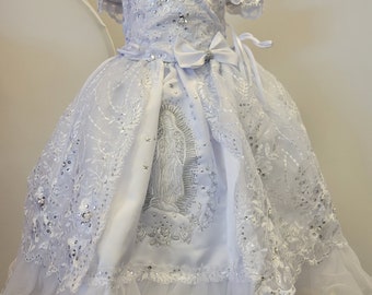 May include: White lace dress with a silver embroidered image of the Virgin Mary. The dress has a satin bodice and a tulle skirt with a lace overlay.