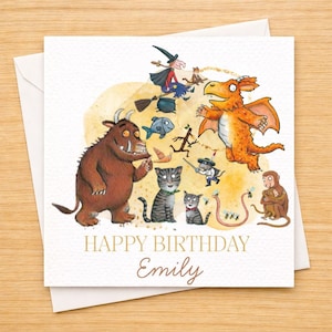 May include: A square greeting card with a watercolor illustration featuring characters from a children's book. The card includes a brown monster, a dragon, cats, and the text "HAPPY BIRTHDAY Emily". The card is on a white envelope.
