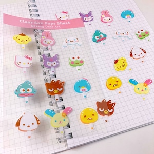 Puede incluir: Una hoja de pegatinas transparentes con varios personajes de dibujos animados en palos de polos. Los personajes incluyen una rana, un perro, un gato, un pingüino y un conejito. El texto "Clear San Pops Sheet Dressy Deer Art" está impreso en la hoja.