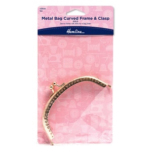 May include: A gold-colored metal bag frame and clasp, 125mm in length, with a curved design. The package includes the text "Metal Bag Curved Frame & Clasp" and "Hemline". The frame is designed to be sewn into a bag and includes links for a chain.