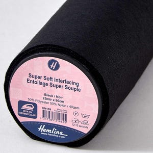 Könnte beinhalten: Eine Rolle schwarzes Super Soft Vlies. Das Etikett lautet "Super Soft Interfacing Entoilage Super Souple" und enthält die Maße 25 Meter x 90 cm. Der Stoff besteht aus 50 % Polyester und 50 % Nylon.