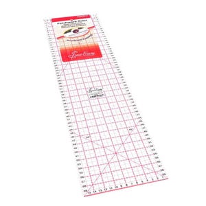 Könnte beinhalten: Ein klarer, rechteckiger Patchwork-Lineal mit roten Gitterlinien und Maßen in Zentimetern. Das Lineal hat ein rot-weißes Etikett mit dem Text "Patchwork Ruler" und "Sew Easy". Das Lineal misst bis zu 150 cm.