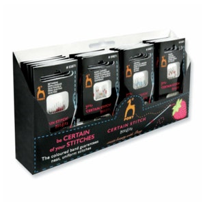 Puede incluir: Una caja de exposición de agujas Pony Certain Stitch. La caja es negra con un logotipo blanco y naranja. Las agujas están empaquetadas en cajas individuales con bandas de colores. El texto en la caja dice "be CERTAIN of your STITCHES. The coloured band guarantees neat, uniform stitches."