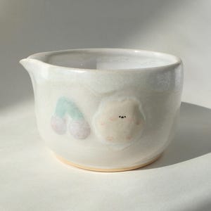 May include: White ceramic jug with a light pink and green cherry design and a small pink bear with a black nose.