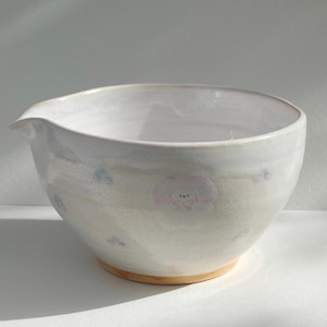 Pode incluir: Uma tigela de cerâmica branca com bico e base clara. A tigela apresenta um padrão floral em rosa e azul. A tigela foi projetada para misturar ingredientes e é adequada para uso na cozinha.