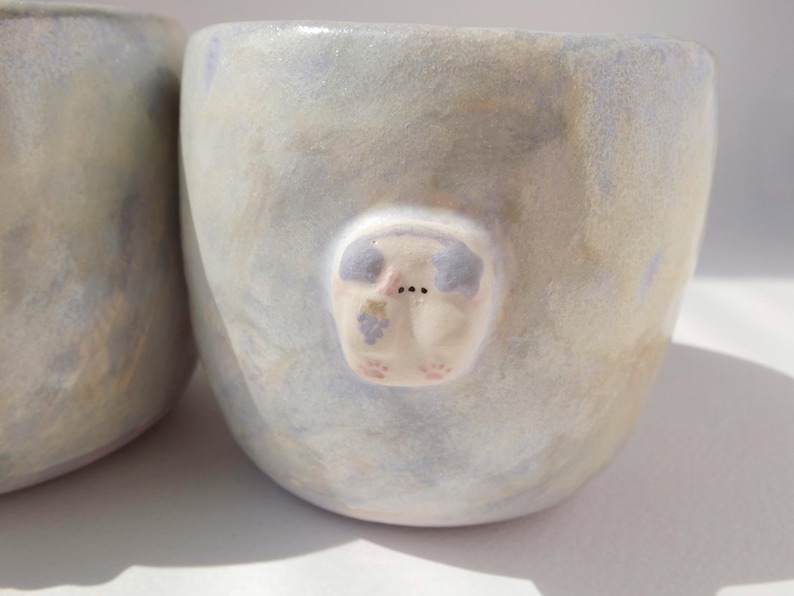 May include: A set of three ceramic mugs with a speckled, matte finish. Each mug features a different color: light blue, cream, and gray. The mugs have a simple, modern design and a comfortable handle.