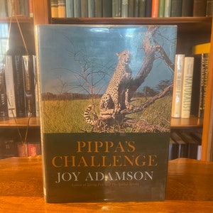 May include: A book cover with a green background and a cheetah sitting on a tree branch. The title of the book is "Pippa's Challenge" by Joy Adamson, author of "Living Free" and "The Spotted Sphinx".