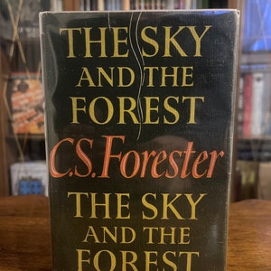 Può includere: Un libro rilegato in nero con lettere dorate. Il titolo è "The Sky and the Forest" di C.S. Forester.